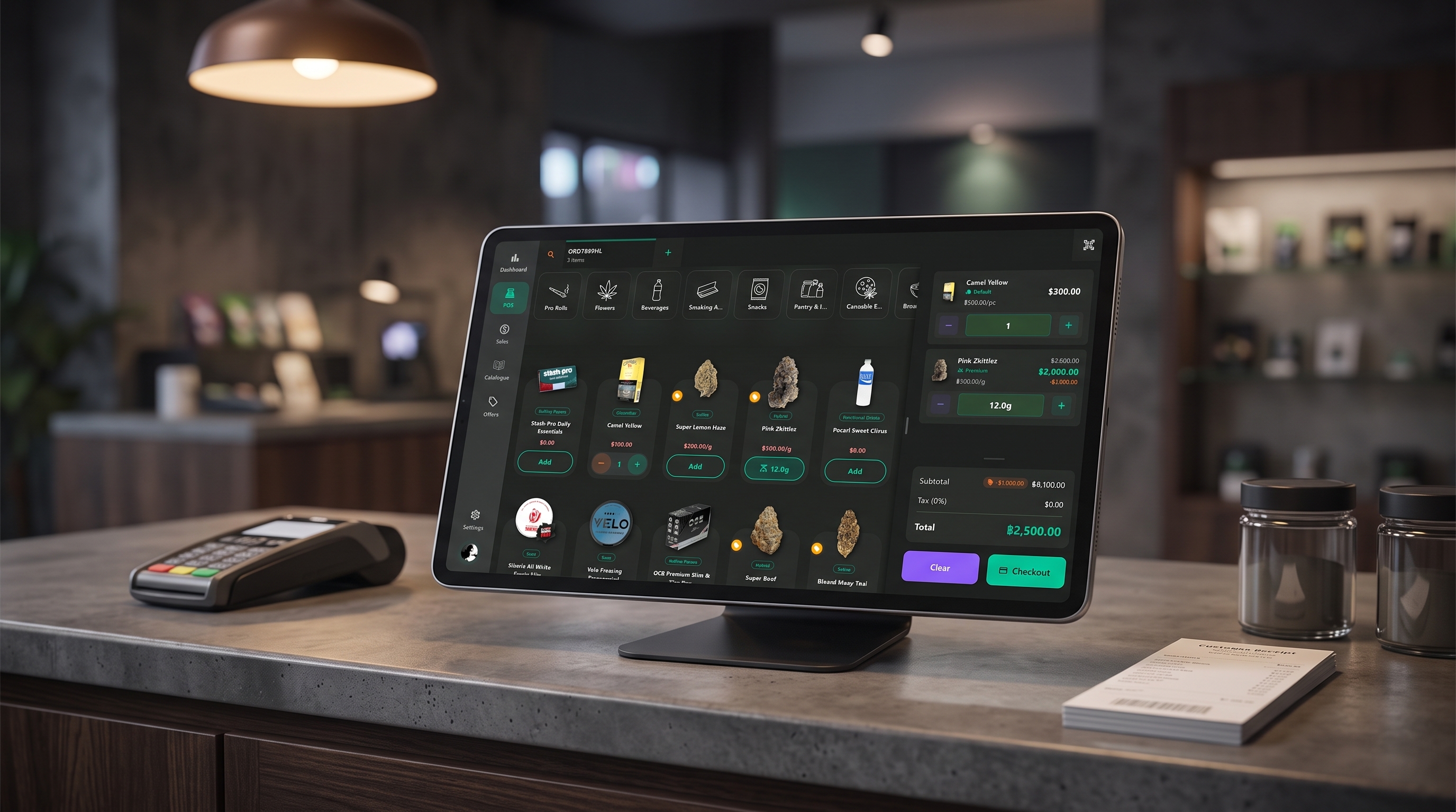 A dispensary counter after closing time with a tablet running the Budy POS on a stand, a card payment terminal, a receipt pad and glass flower jars under a warm pendant lamp