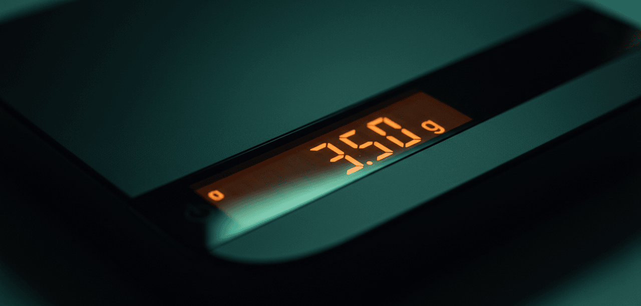 Macro close-up of the Acaia Lunar orange LCD showing grams, with jade-green ambient glow